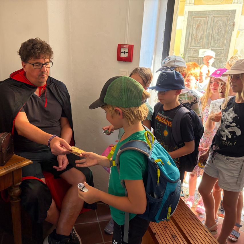 Mann mit Umhang gibt einem Buben mit Rucksack eine Karte in einem Museum in Österreich.