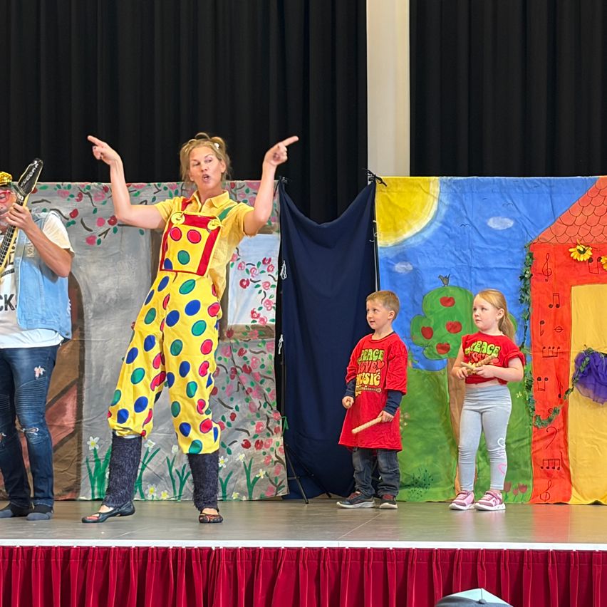 Künstlerin mit bunter Latzhose und Kinder auf Bühne mit gemalter Dekoration