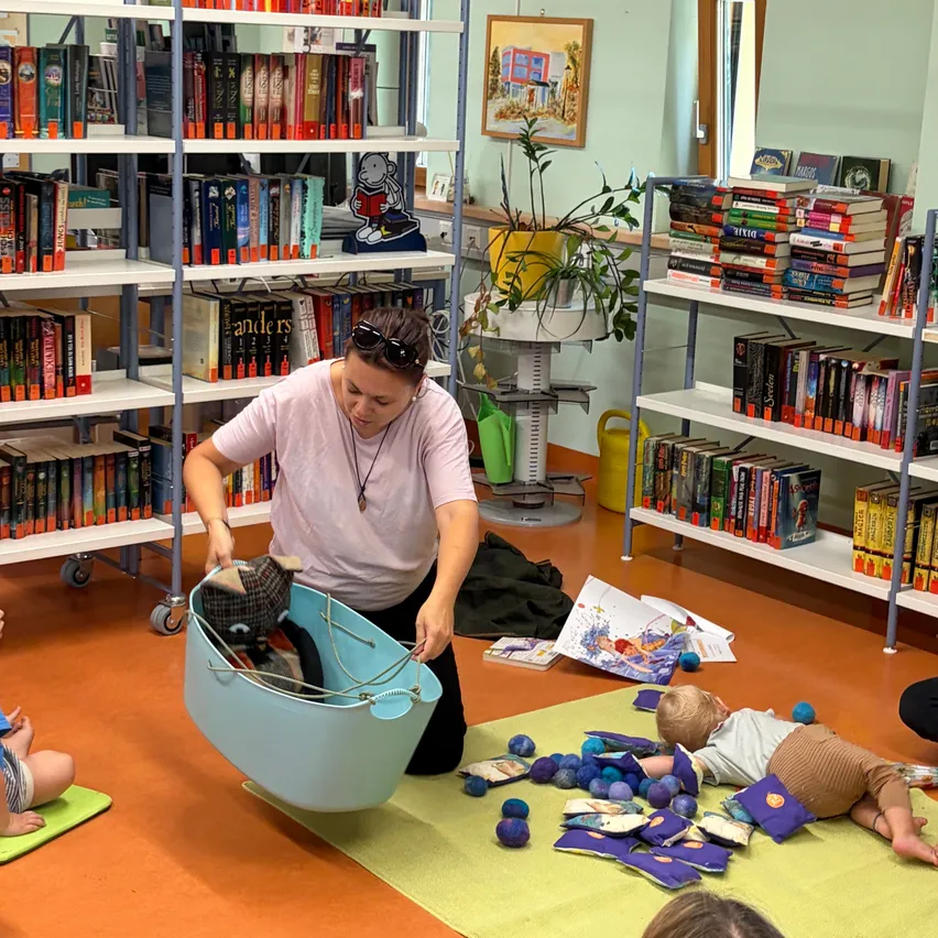 Eine Frau in einer Bibliothek mit einem Baby auf dem Boden und einem Korb mit Spielzeug.