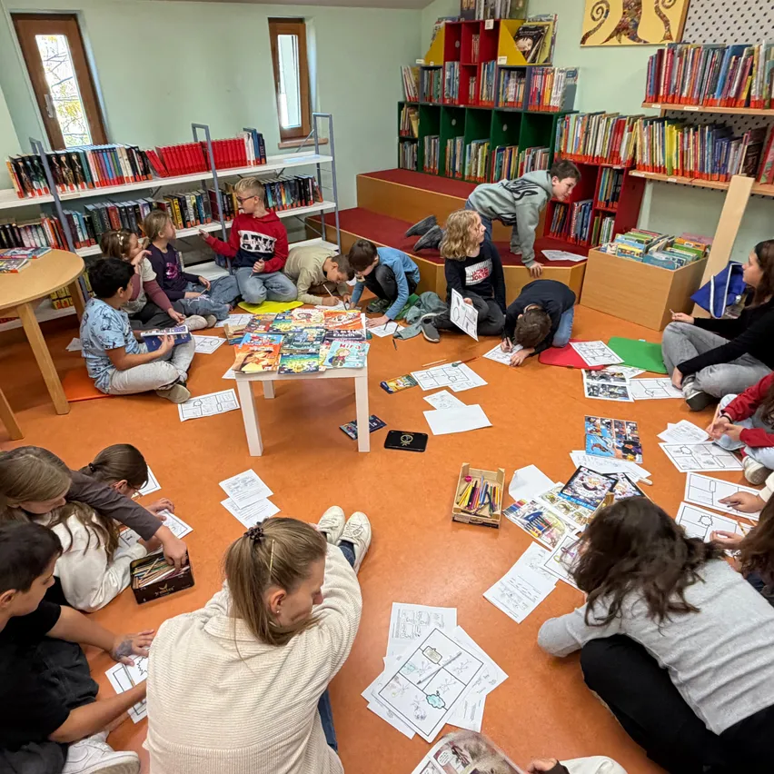 Eine Gruppe von Kindern sitzt auf dem Boden in einer Bibliothek und beschäftigt sich mit Lesen und Schreiben.