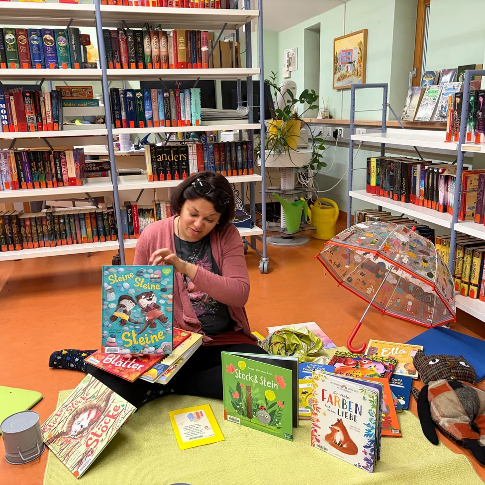 Eine Frau sitzt auf dem Boden in einer Bibliothek und hält ein Buch mit dem Titel Steine Steine.