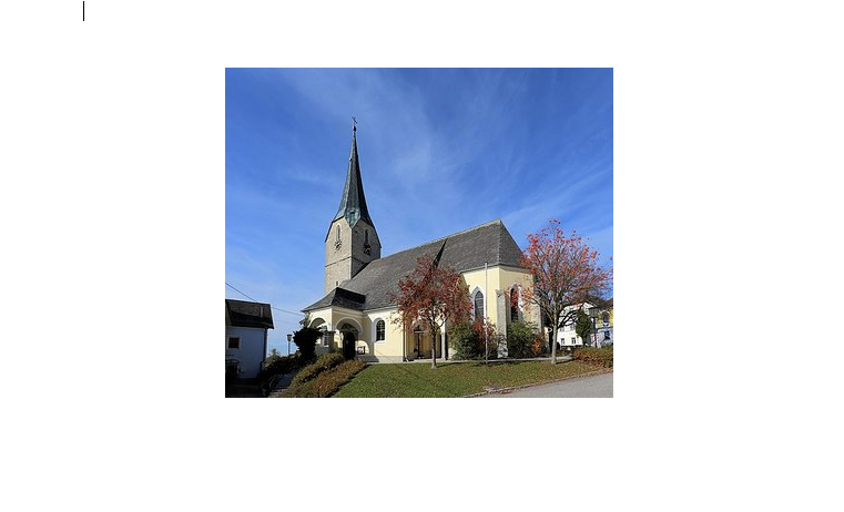 Eine kleine Kirche mit einem Kirchturm und einem Glockenturm, vor einem blauen Himmel, umgeben von Grün und Bäumen.
