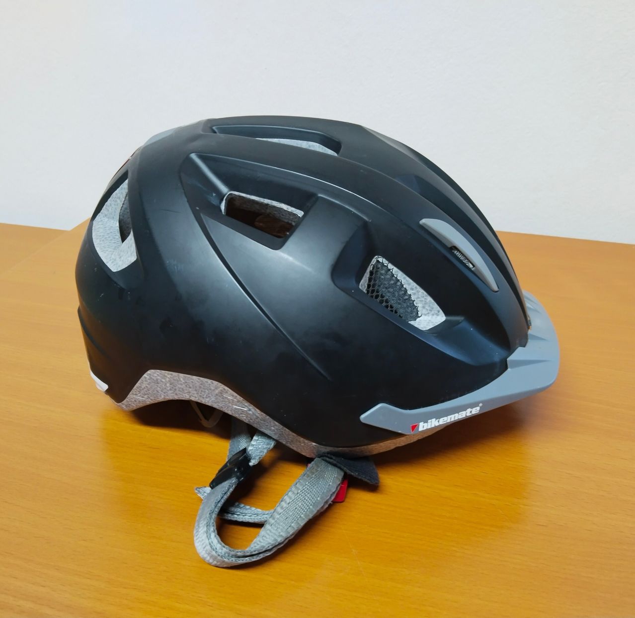 Ein schwarzer Fahrradhelm mit grauen Akzenten und der Marke 'bikemate' steht auf einem Holztisch.