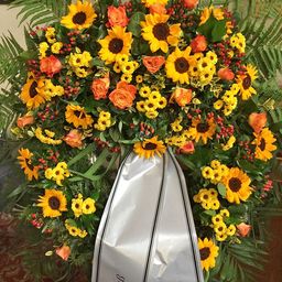 Ein runder Kranz mit Sonnenblumen, Rosen und grünen Blättern mit einem silbernen Band in der Mitte.