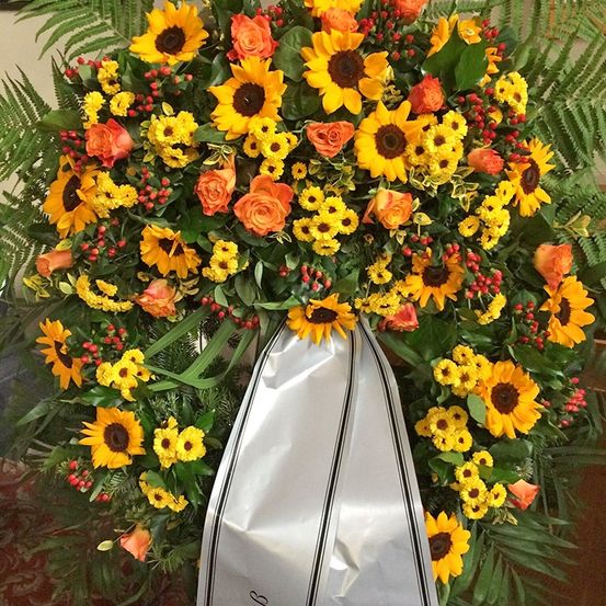 Ein runder Kranz mit Sonnenblumen, Rosen und grünen Blättern mit einem silbernen Band in der Mitte.