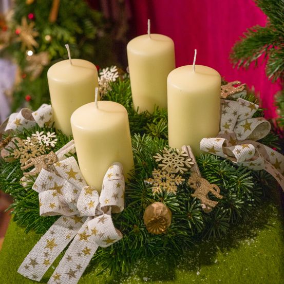 Ein Kranz mit vier weißen Kerzen, verziert mit Schneeflocken, Schleifen und Sternen, auf einer grünen Oberfläche platziert.