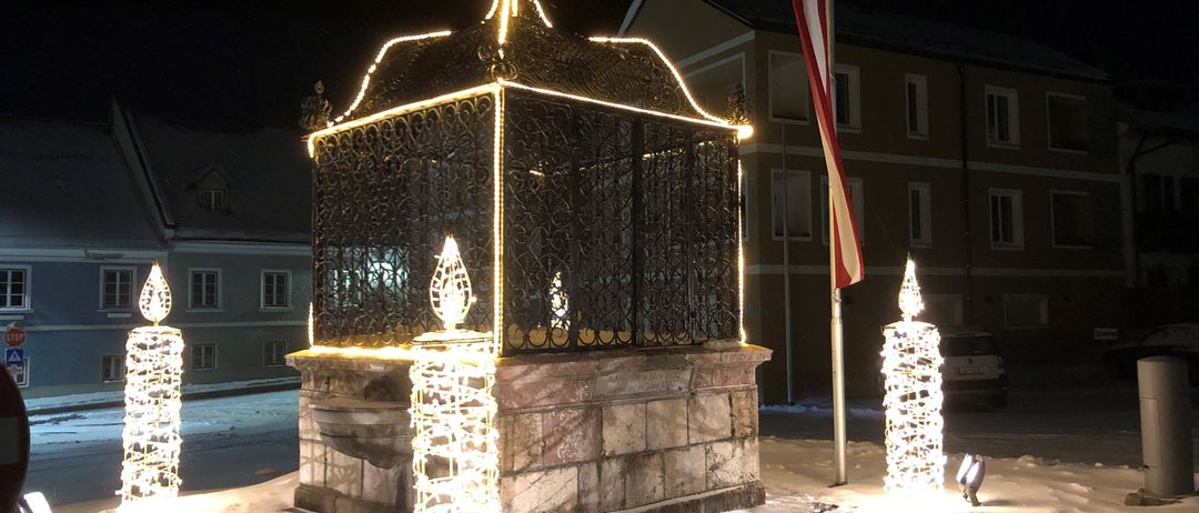 Ein wunderschön beleuchteter Brunnen bei Nacht mit Schnee auf dem Boden.