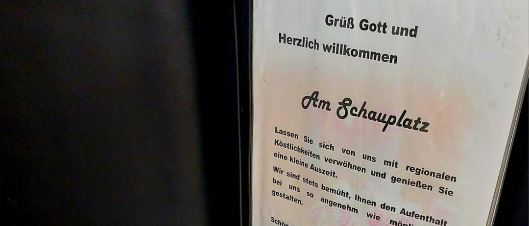 Ein Teller mit gegrillten Rippchen, Pommes, Sauerkraut und einer roten Sauce. Im Hintergrund befindet sich ein Menübrett mit regionalen Gerichten.