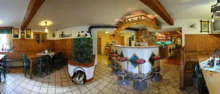 A cozy restaurant with wooden walls, a tiled floor, and a counter with stools. A wooden table with chairs is set up, and a wooden cabinet is placed on the left. A framed picture is mounted on the wall. A green stove is on the left, and a lamp is mounted on the ceiling.