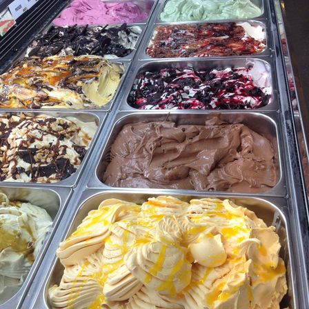 Verschiedene Eissorten sind in einer Vitrine ausgestellt, darunter Schokolade, Vanille und fruchtaromatisiertes Eis.