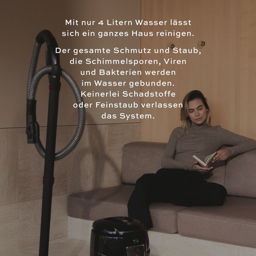 Eine Frau liest ein Buch, während sie auf einer Couch sitzt, mit einem Staubsauger in der Nähe. Der Staubsauger ist mit einem Schlauch verbunden, was darauf hindeutet, dass er gerade zum Reinigen verwendet wird. Das Bild vermittelt eine Botschaft über die Effektivität des Staubsaugers bei der Entfernung von Schmutz und Allergenen.