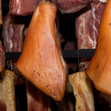 Nahaufnahme von geräucherten Fleischstücken in einer Fleischerei, mit verschiedenen Schnitten und rauchiger, rustikaler Erscheinung.