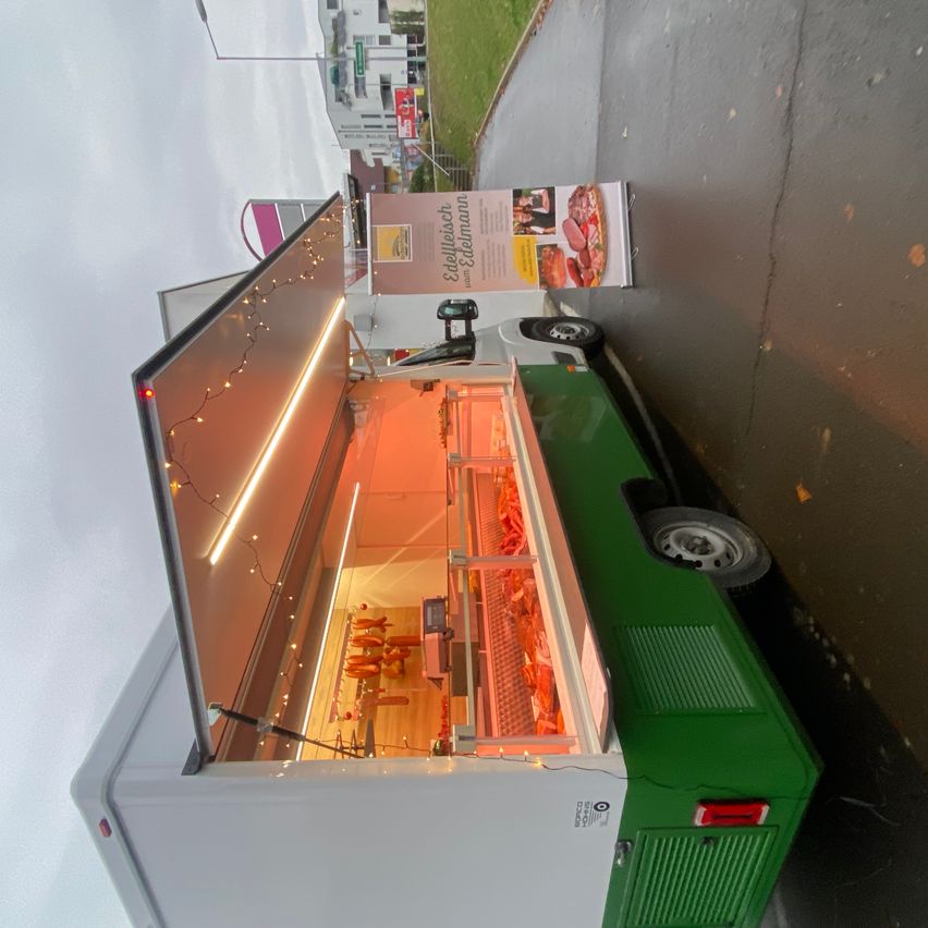 Eine Draufsicht auf einen grünen und weißen Imbisswagen, der auf einer Straße geparkt ist, mit geöffneter Tür, die einen beleuchteten Innenraum und ein nahes Menübrett zeigt.