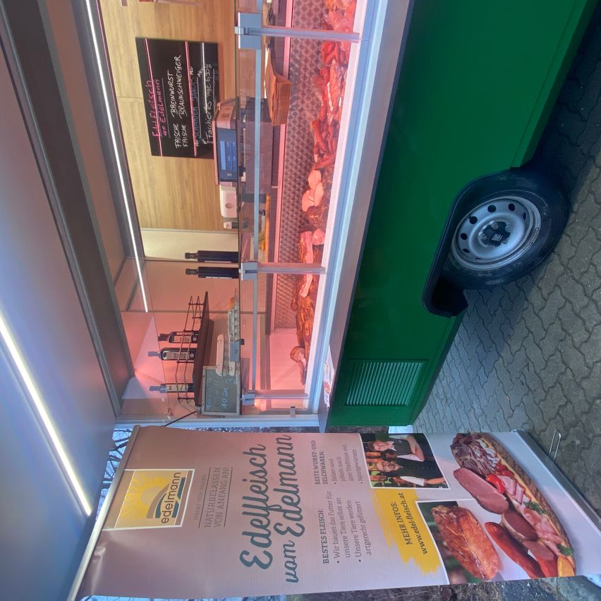 Ein Fleischgeschäft ist geöffnet und zeigt Fleisch hinter einer Glastheke an. Der Laden hat Holzböden und ein schwarzes Schild. Ein Poster für Edelweisch van Edelmann ist davor, mit Fleisch und der Website des Geschäfts.