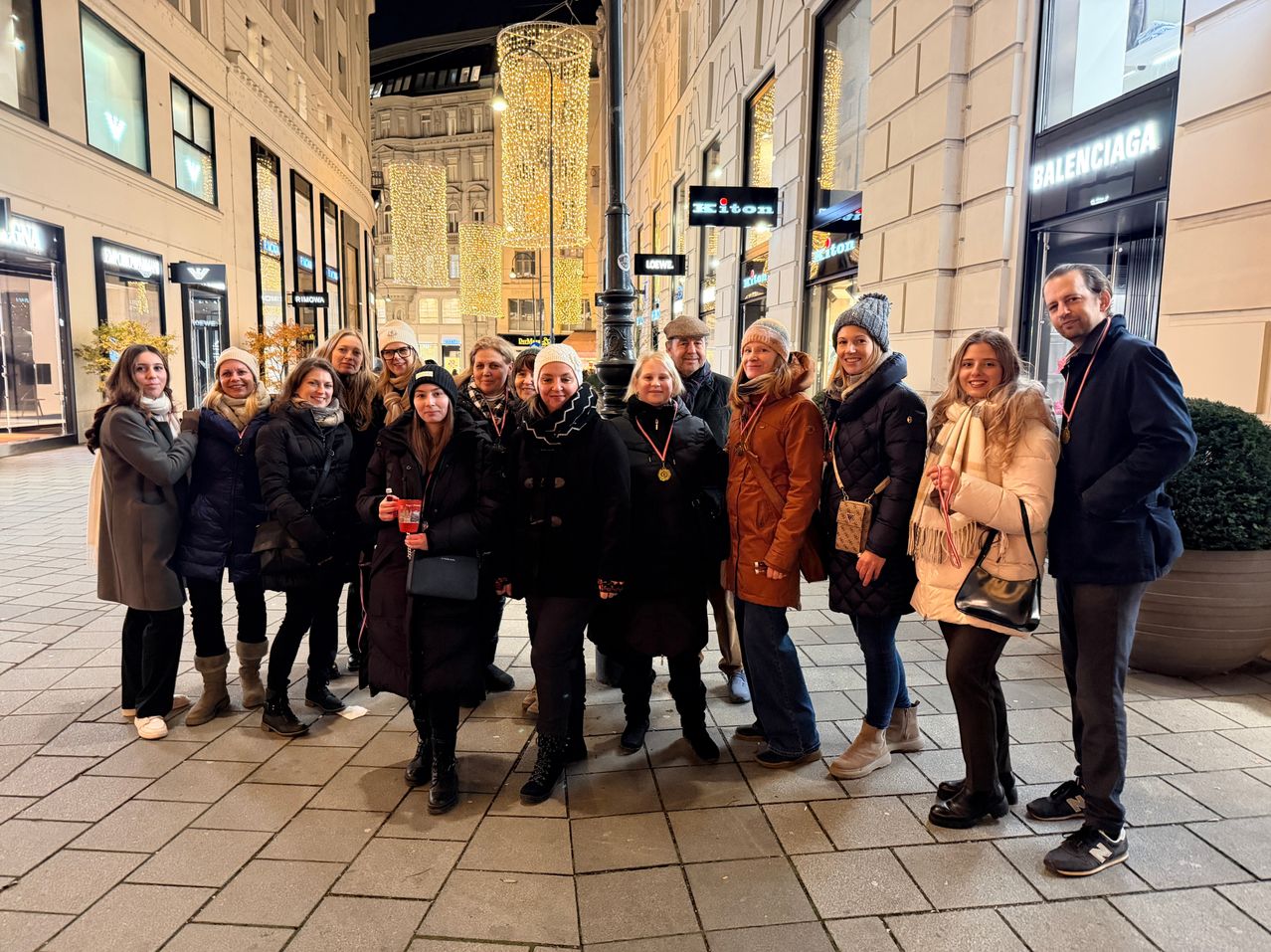 Eine Gruppe von Menschen in Winterkleidung posiert für ein Foto vor einem Gebäude mit dem Schild 'Balenciaga'.