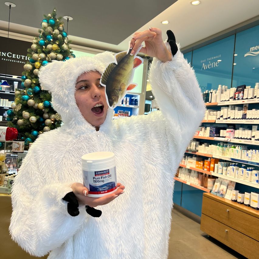 Eine Person in einem weißen pelzigen Kostüm hält einen Fischausschnitt und eine Dose Fischöl in einem Geschäft mit einem Weihnachtsbaum im Hintergrund.