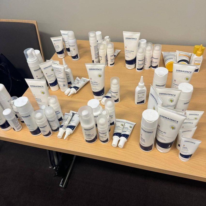 Ein Holztisch mit verschiedenen Dermasence-Hautpflegeprodukten, darunter Flaschen, Tuben und Gläser, ordentlich angeordnet. Die Produkte haben verschiedene Farben und Größen, wobei einige weiße Kappen und andere blaue haben.