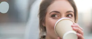 Eine Frau trinkt aus einem weißen Becher mit ernster Miene. Der Hintergrund ist unscharf.