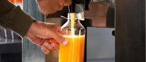 Eine Person füllt eine Orangensaftflasche mit einem Spender in einer kommerziellen Umgebung.