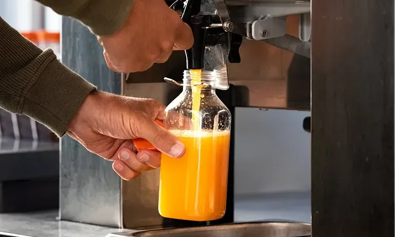 Eine Person füllt eine Orangensaftflasche mit einem Spender in einer kommerziellen Umgebung.