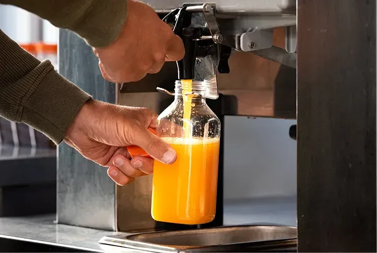 Eine Person füllt eine Orangensaftflasche mit einem Spender in einer kommerziellen Umgebung.
