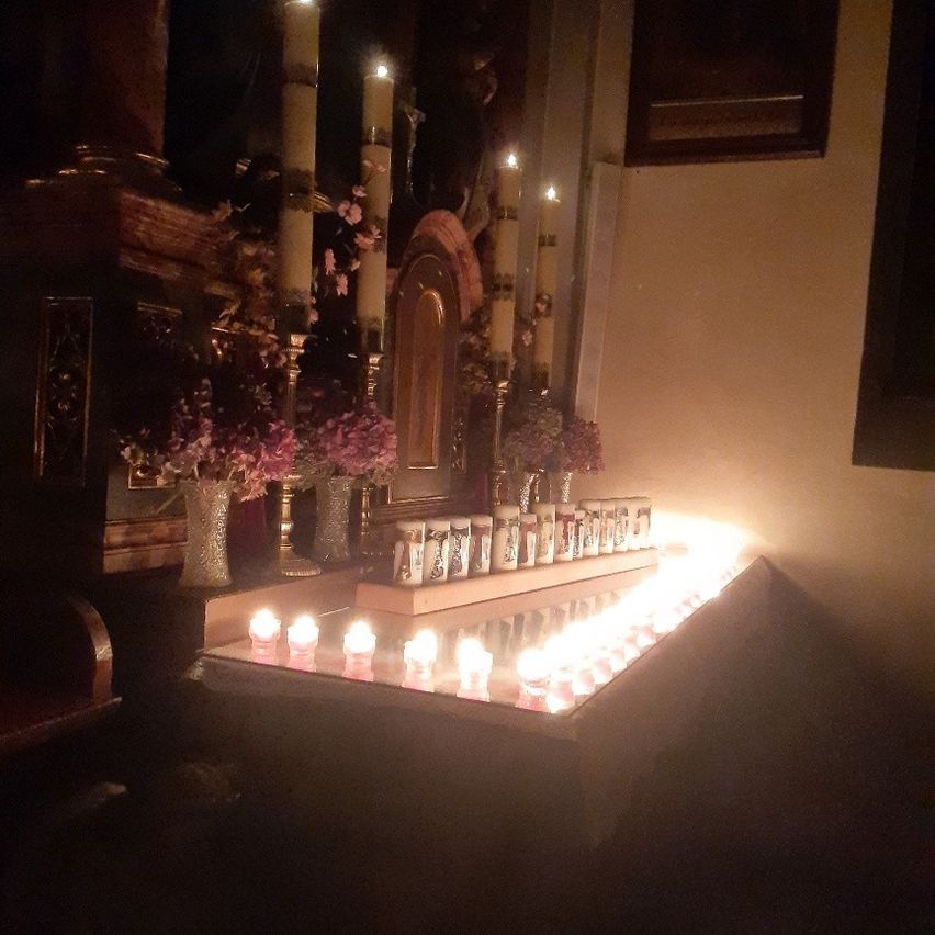 Ein schwach beleuchteter Raum mit Kerzen und Blumen auf einem Tisch vor einer religiösen Ikone.