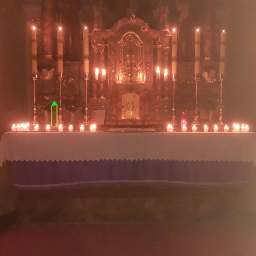 Ein Altar mit zahlreichen Kerzen darum herum, einem grünen Kristall in der Mitte und einem goldenen Altarbild dahinter.