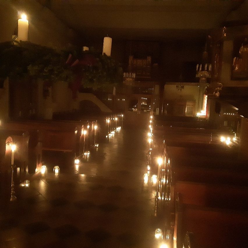 Ein schwach beleuchteter Kirchengang mit Reihen von brennenden Kerzen auf beiden Seiten, die zu einem Altar mit einer großen Kerze führen.