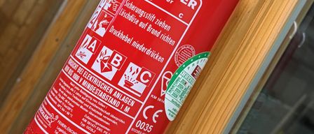 Ein roter Feuerlöscher mit weißen Text, gekennzeichnet durch GOCKLER, an einer Holzwand montiert. Er hat ein Druckmessgerät und einen roten Griff.