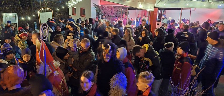 Eine nächtliche Versammlung von Menschen im Freien, einige in Kostümen, in der Nähe eines dekorierten Gebäudes mit Lichterketten.