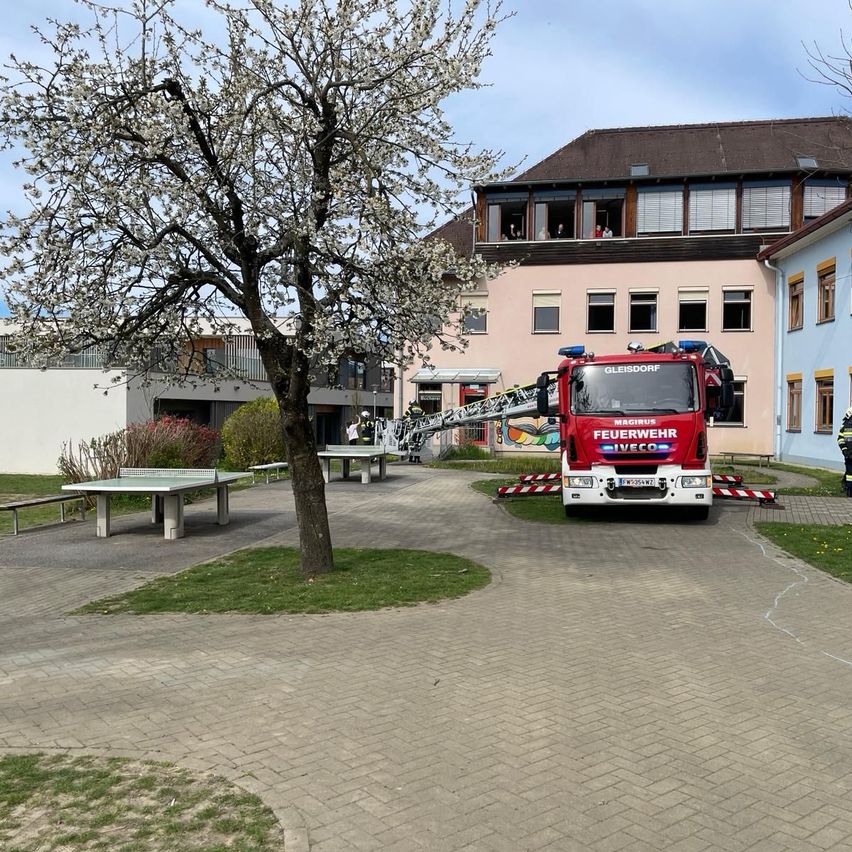 Ein roter Feuerwehrwagen mit der Aufschrift "Magirus" auf der Seite ist vor einem Gebäude geparkt, wobei eine Leiter ausgeklappt ist.