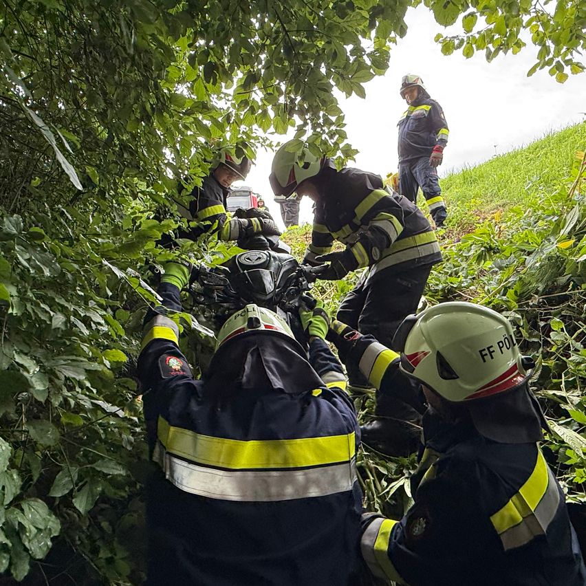 Feuerwehrleute retten jemanden aus einem Fahrzeug, das in einem Busch stecken geblieben ist. Sie tragen alle Schutzausrüstung.