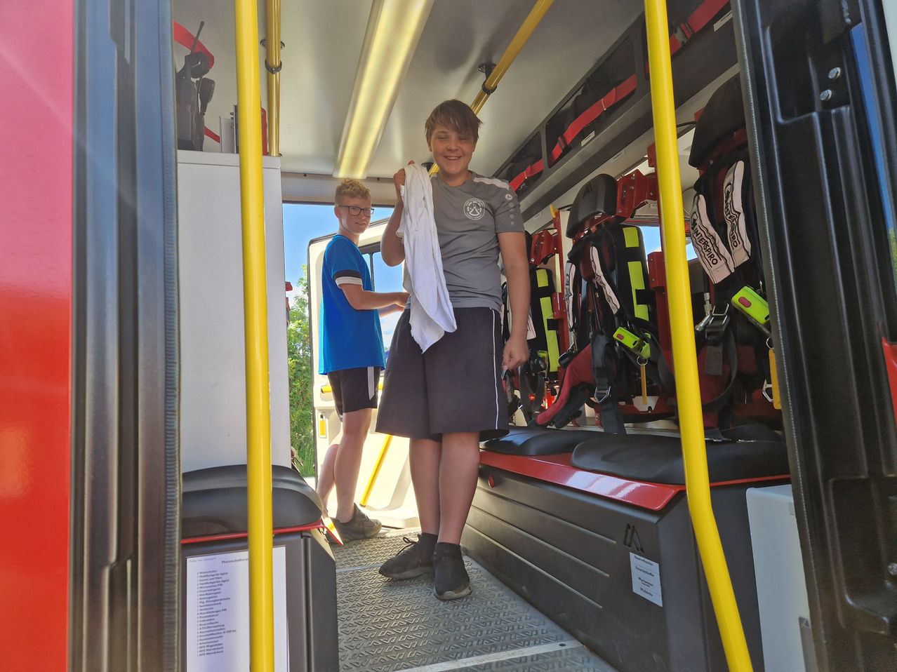 Zwei Jungen stehen in einem Krankenwagen mit medizinischer Ausrüstung, einer hält ein weißes Handtuch, während der andere eine Brille und ein blaues Hemd trägt.
