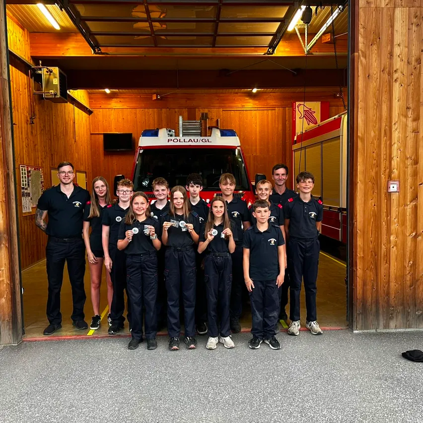 Eine Gruppe von Kindern und Erwachsenen posiert für ein Foto vor einem Feuerwehrwagen in einem Feuerwehrhaus.