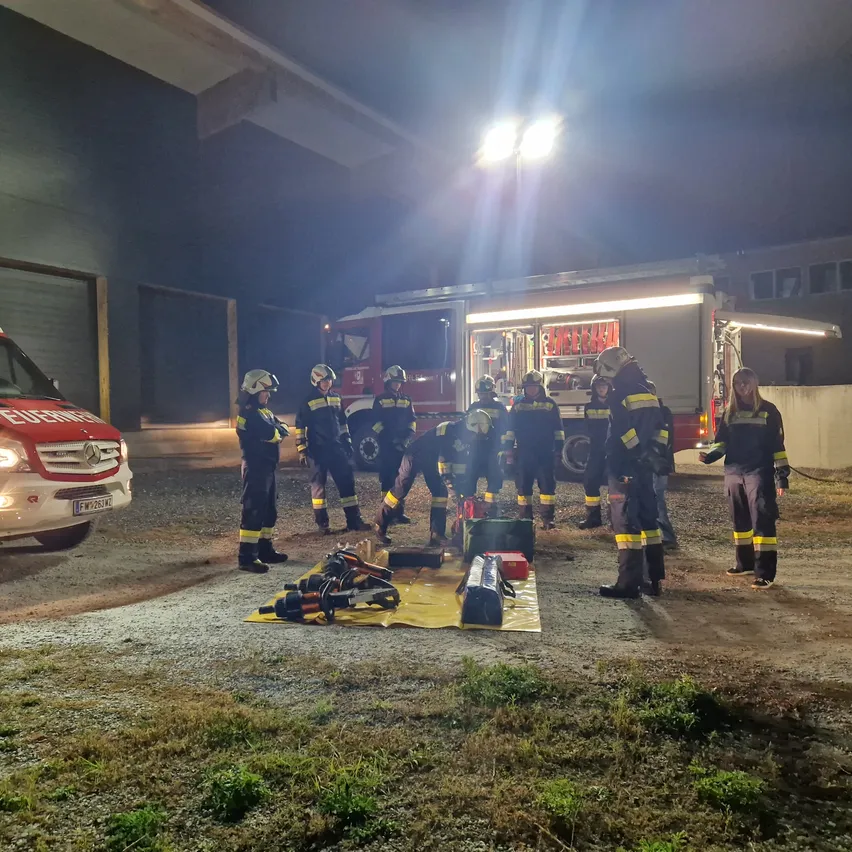 Eine Gruppe von Feuerwehrleuten in Uniform versammelt sich bei Nacht um einen Feuerwehrwagen.