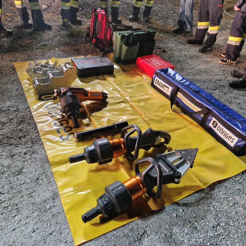 Eine Gruppe von Feuerwehrleuten ist um ein gelbes Tuch mit verschiedenen Werkzeugen und Ausrüstungsgegenständen versammelt.