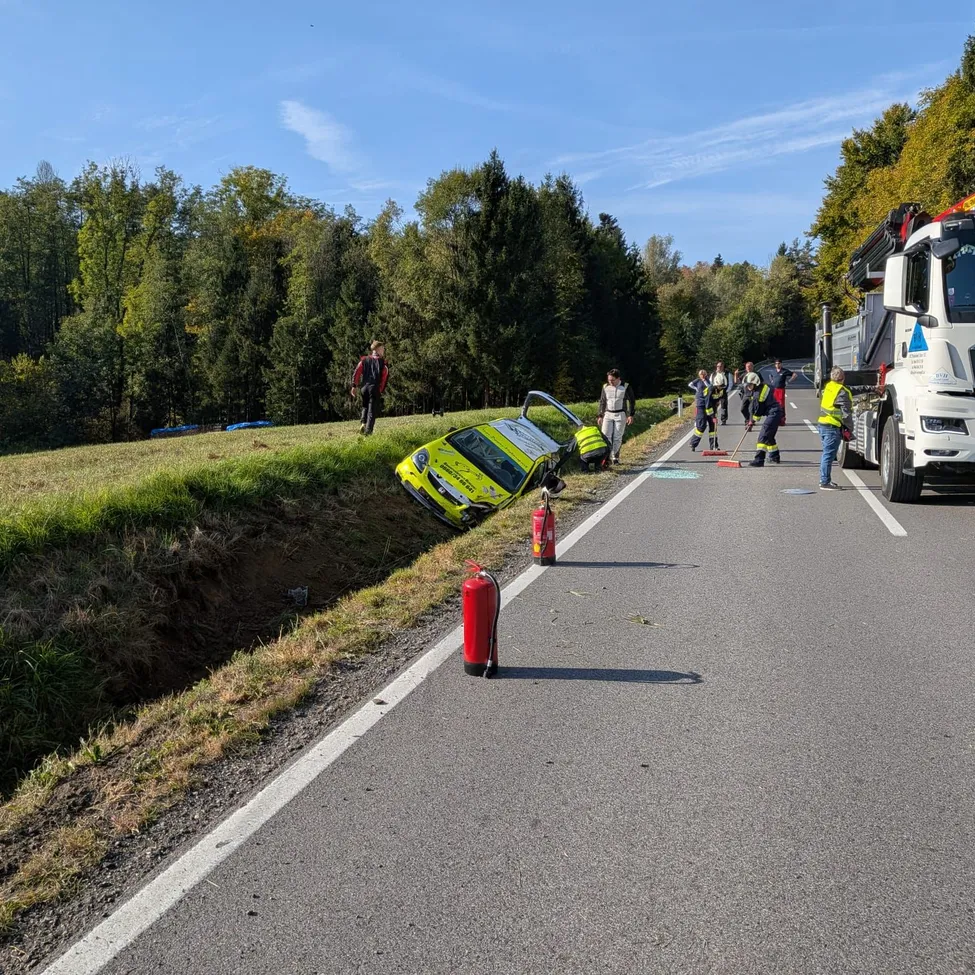 Ein gelbes Auto ist auf der Straßenseite umgekippt. Ein Lastwagen ist auf der Seite geparkt, und mehrere Leute stehen darum herum.