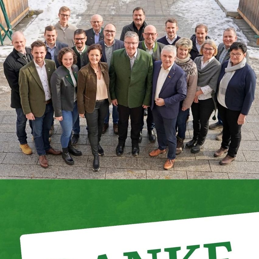 Eine Gruppe von Menschen in Winterkleidung posiert für ein Foto im Freien. Hinter ihnen befindet sich ein Holzzaun und etwas Schnee ist sichtbar.