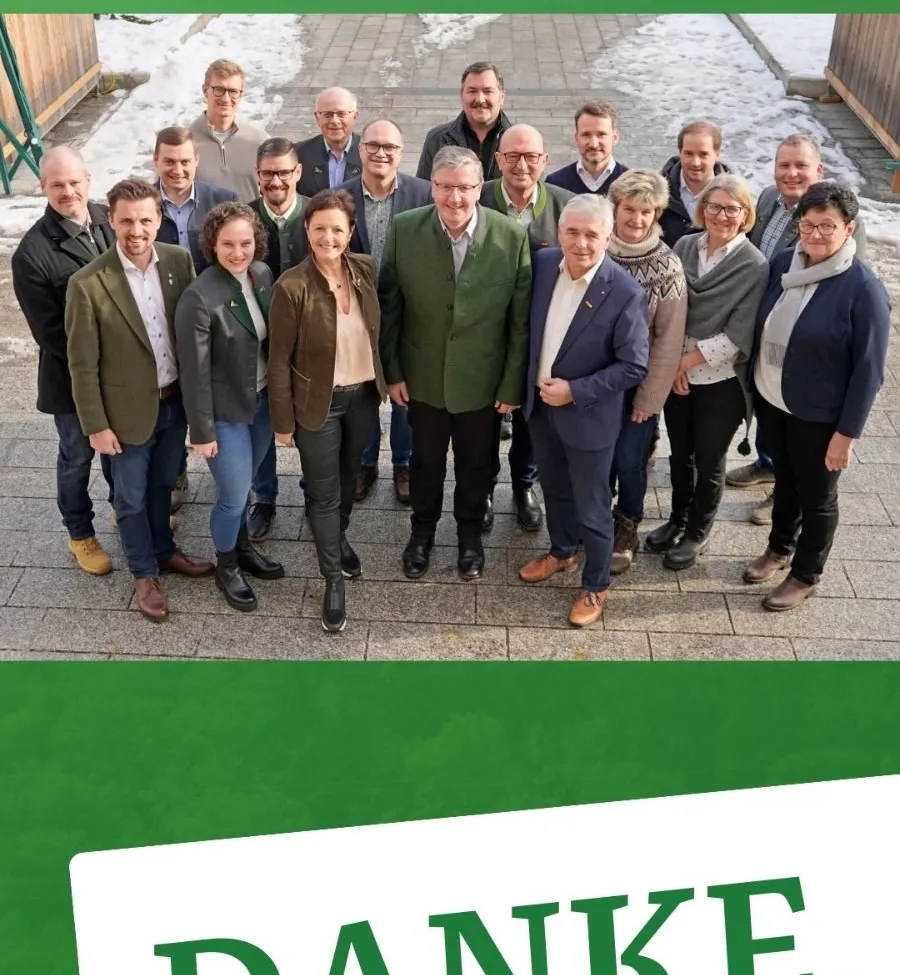 Eine Gruppe von Menschen in Winterkleidung posiert für ein Foto im Freien. Hinter ihnen befindet sich ein Holzzaun und etwas Schnee ist sichtbar.