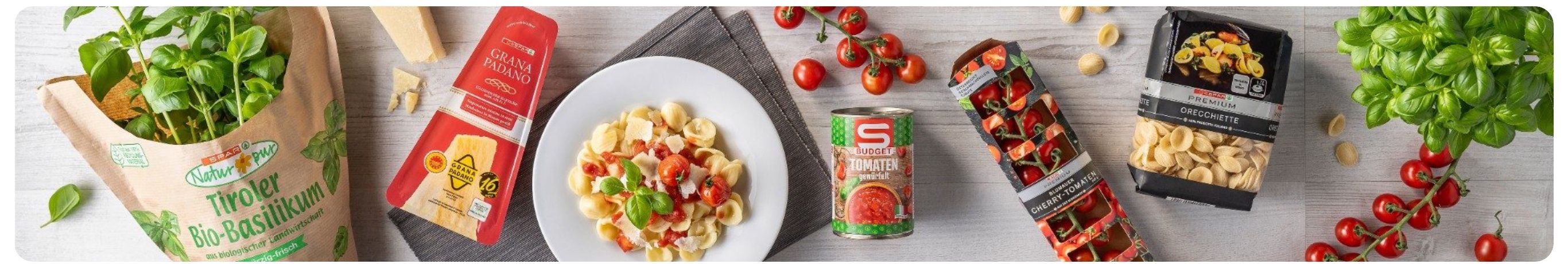 Ein Teller mit Nudeln, Tomaten und Basilikum auf einem Holztisch. Eine Dose Budget Tomaten neben dem Teller.