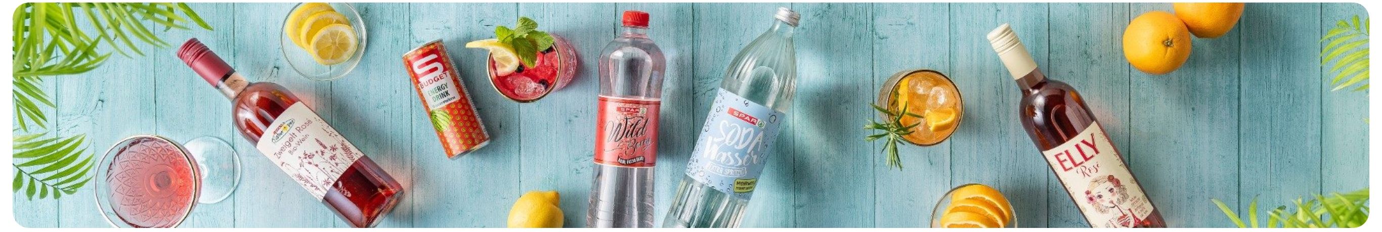 Zwei Flaschen Limonade mit roten und blauen Etiketten, eine Zitrone und ein Getränk mit Eis und Minzblättern auf blauem Hintergrund.