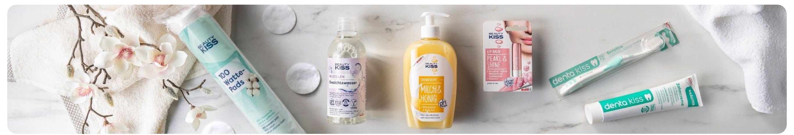 Drei Schönheitsprodukte von Beauty Kiss, darunter Mizellenwasser, eine Creme mit Honig und ein Lippenbalsam, liegen auf einer Marmoroberfläche.