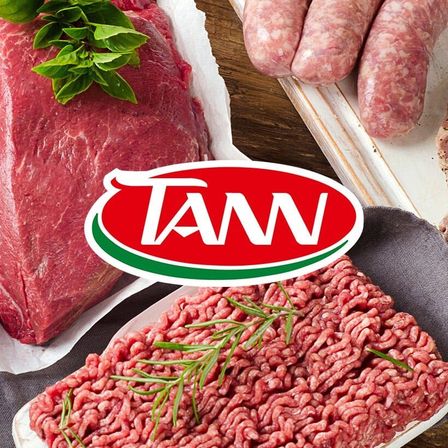 Rohes Rindfleisch und Hackfleisch mit Kräutern und Würsten auf einem Holztisch. TAN-Logo in Rot und Grün.