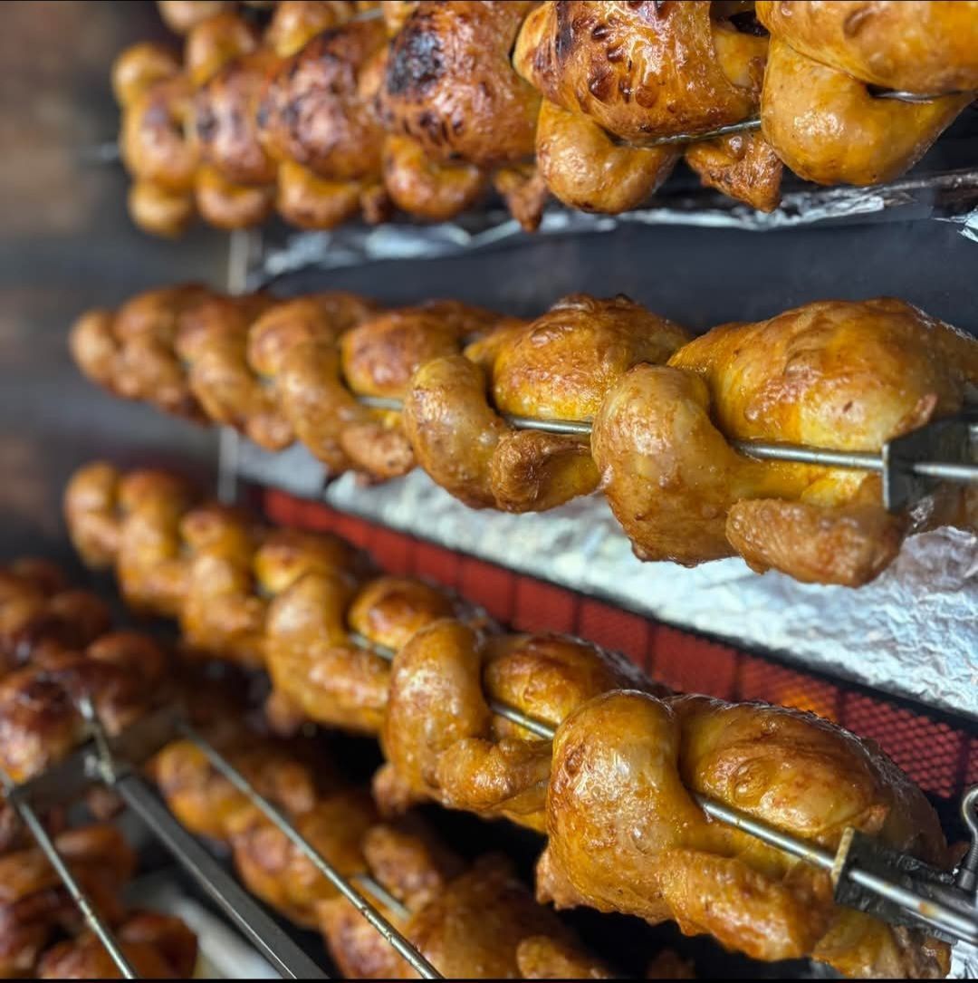 Mehrere Roste mit gebratenem Huhn auf einem Gestell, mit goldbrauner Farbe und knuspriger Haut, in einer professionellen Küche zubereitet.