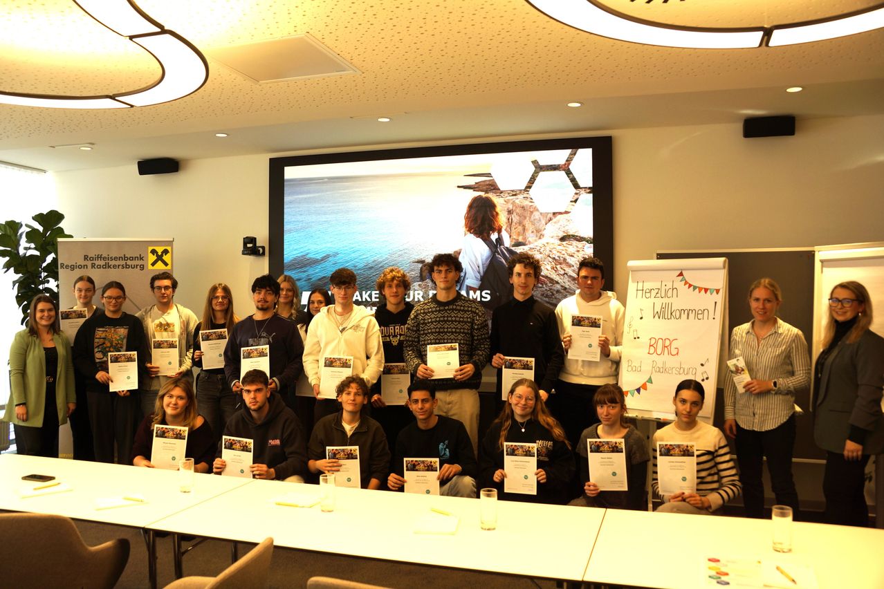 Eine Gruppe junger Menschen, die Zertifikate halten, posiert für ein Foto in einem Konferenzraum. Dahinter befindet sich eine Projektionsleinwand mit einer landschaftlichen Szene. Ein Banner mit Musiknoten und dem Text 'BORG' steht rechts.