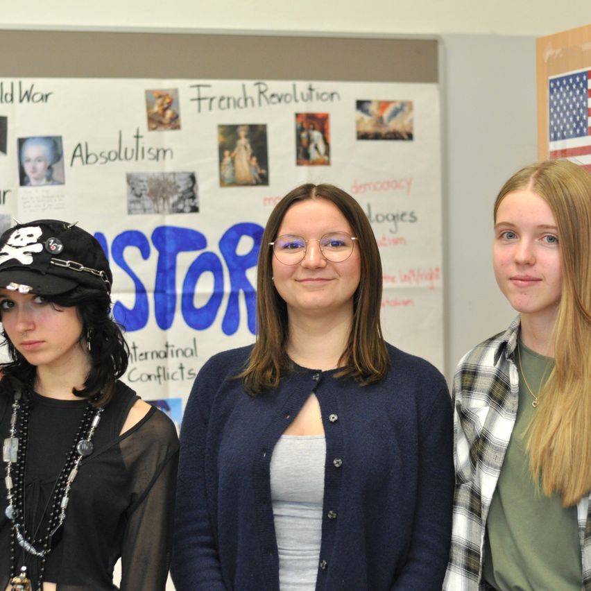 Drei Mädchen stehen vor einem Bulletin-Board mit historischen Themen. Ein Mädchen mit einer Piratenmütze lächelt.