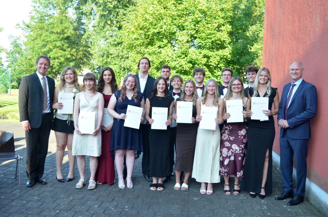 Eine Gruppe von Menschen in formeller Kleidung mit Zertifikaten posiert im Freien für ein Foto am Tag.