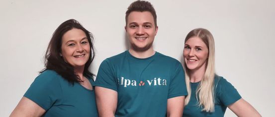 Three individuals, two women and a man, are posing for a photo. They are all wearing matching teal shirts. The man has a logo on his shirt.