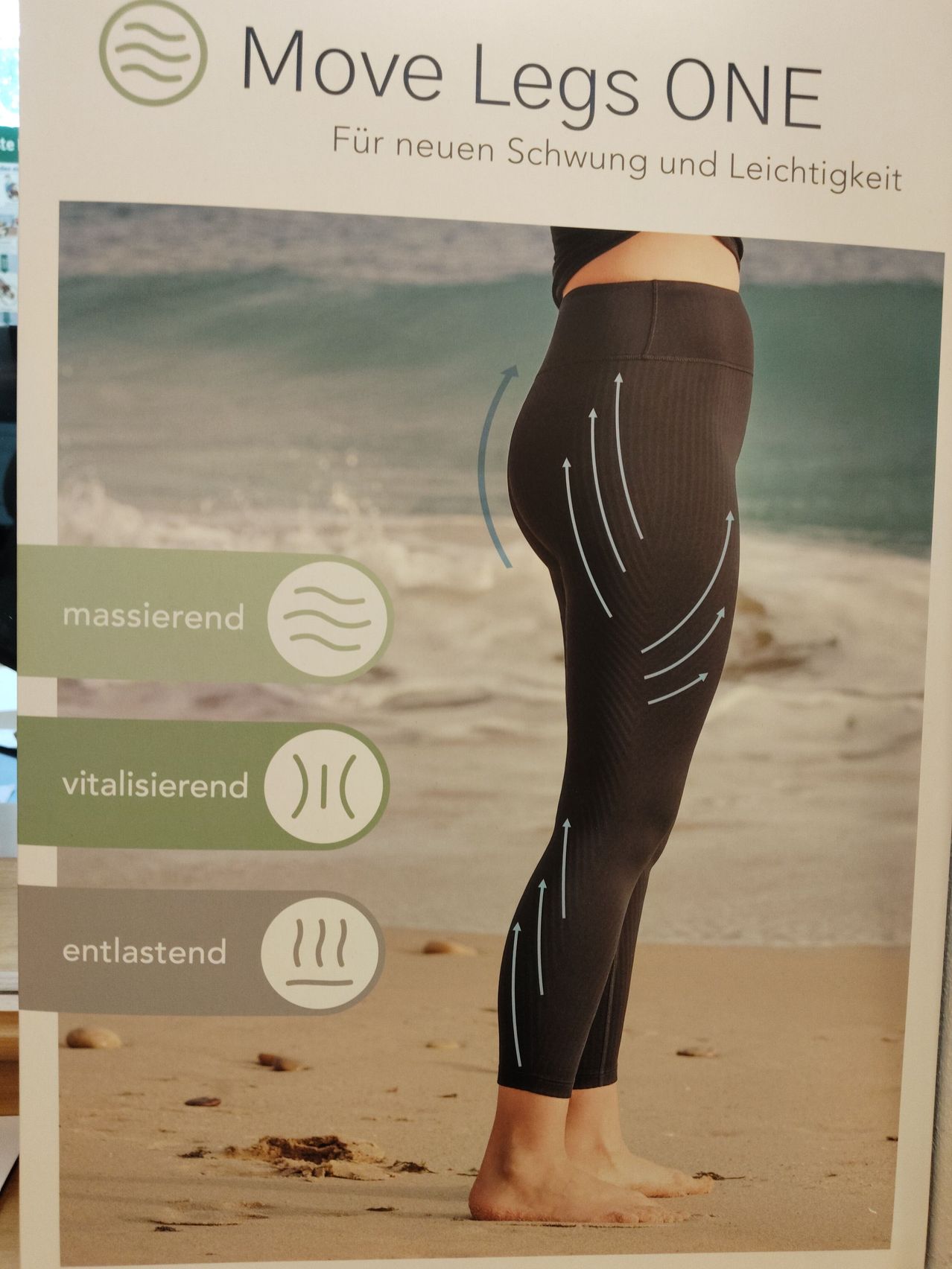 Eine Werbung für Kompressionsleggings mit einer Frau am Strand. Die Leggings haben Pfeile, die nach oben zeigen, und sind beschriftet mit 'massierend', 'vitalisierend' und 'entlastend'.