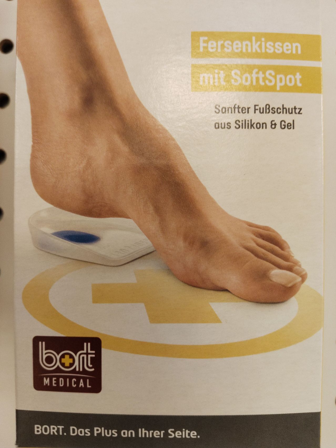 A foot resting on a white scale with a yellow cross symbol, on a white background with a yellow border. The text reads 'mit SoftSpot' and 'Sanfter Fußschutz aus Silikon & Gel'. The brand name 'bort MEDICAL' is visible at the bottom.